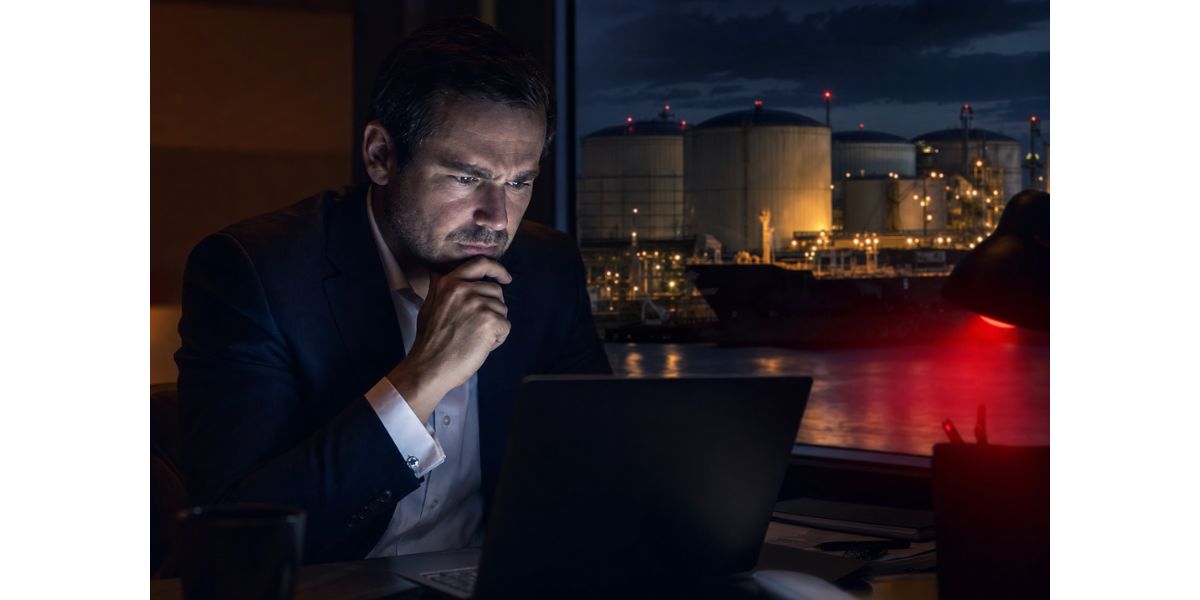 Petroleum trader reviewing transaction documents on a laptop while overlooking illuminated fuel storage tanks and an oil terminal at night, representing due diligence, fraud prevention, and risk management in global fuel trading.